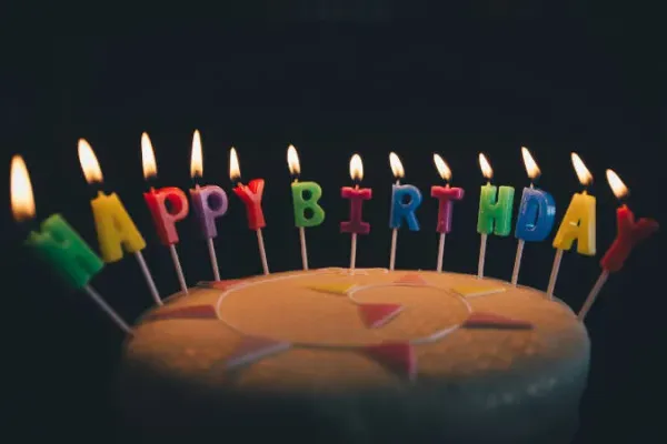 Ein Kuchen mit brennenden Kerzen darauf. Die Kerzen bilden den Schriftzug "Happy Birthday".