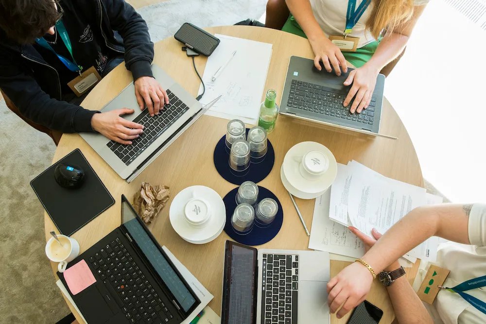 mehrere Laptops auf einem Tisch mit Händen von drei Menschen auf den jeweiligen Tastaturen