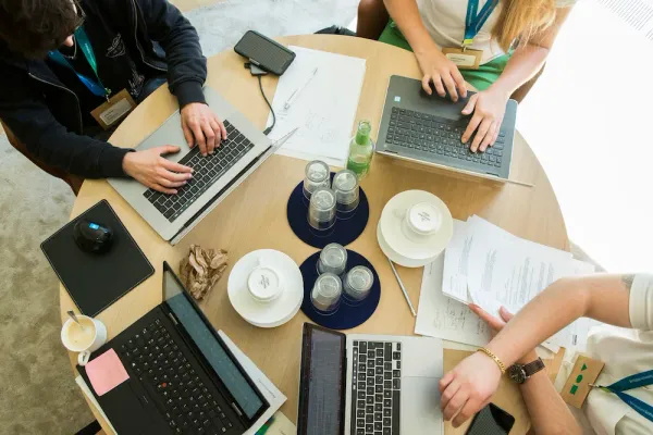 mehrere Laptops auf einem Tisch mit Händen von drei Menschen auf den jeweiligen Tastaturen