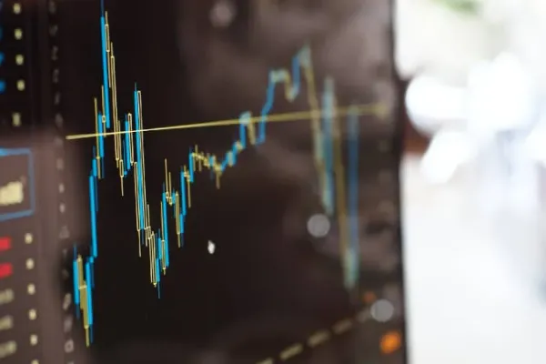 Ein Computer-Monitor leicht von der Seite fotografiert. Er zeigt ein Dashboard mit einem Liniendiagramm, welches eine blaue und eine gelbe Linie enthält. Neben dem Liniendiagramm sind verschwommen weitere Zahlen und Elemente zu sehen. 