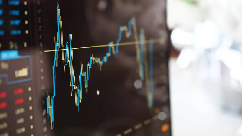 Ein Computer-Monitor leicht von der Seite fotografiert. Er zeigt ein Dashboard mit einem Liniendiagramm, welches eine blaue und eine gelbe Linie enthält. Neben dem Liniendiagramm sind verschwommen weitere Zahlen und Elemente zu sehen. 