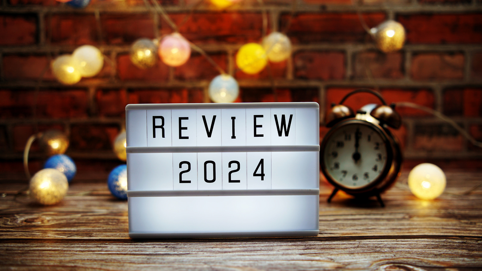 picture shows a sign that says "review 2024" in the background are some small lights and a clock