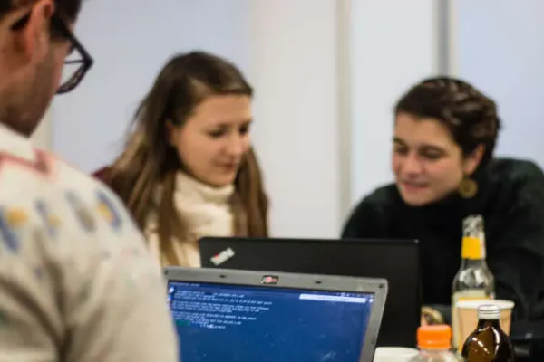 Man sieht mehrere Personen, die zusammensitzen und gemeinsam an zwei Laptops arbeiten.