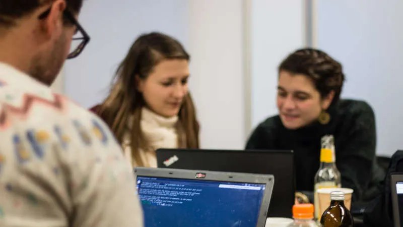 Man sieht mehrere Personen, die zusammensitzen und gemeinsam an zwei Laptops arbeiten.