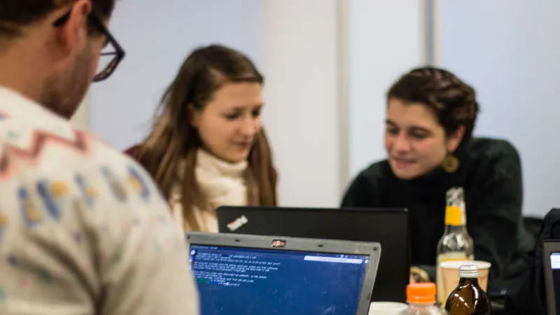 Man sieht mehrere Personen, die zusammensitzen und gemeinsam an zwei Laptops arbeiten.