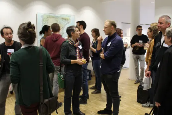 In einem hellen Veranstaltungsort stehen viele Menschen mit Namensschildern und unterhalten sich angeregt.