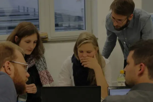 eine Gruppe von Personen zwischen 20 und 30 Jahren sitzt an einem Tisch und schaut auf einen Laptop.