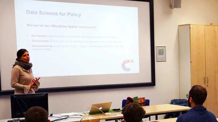 Eine Person hält einen Vortrag. Der Titel der Folie, die an eine Leinwand geworfen ist, ist "Data Science for Policy".  Unten rechts auf der Folie ist das CorrelAidX Logo zu sehen.