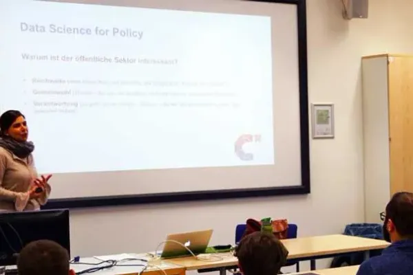 Eine Person hält einen Vortrag. Der Titel der Folie, die an eine Leinwand geworfen ist, ist "Data Science for Policy".  Unten rechts auf der Folie ist das CorrelAidX Logo zu sehen.