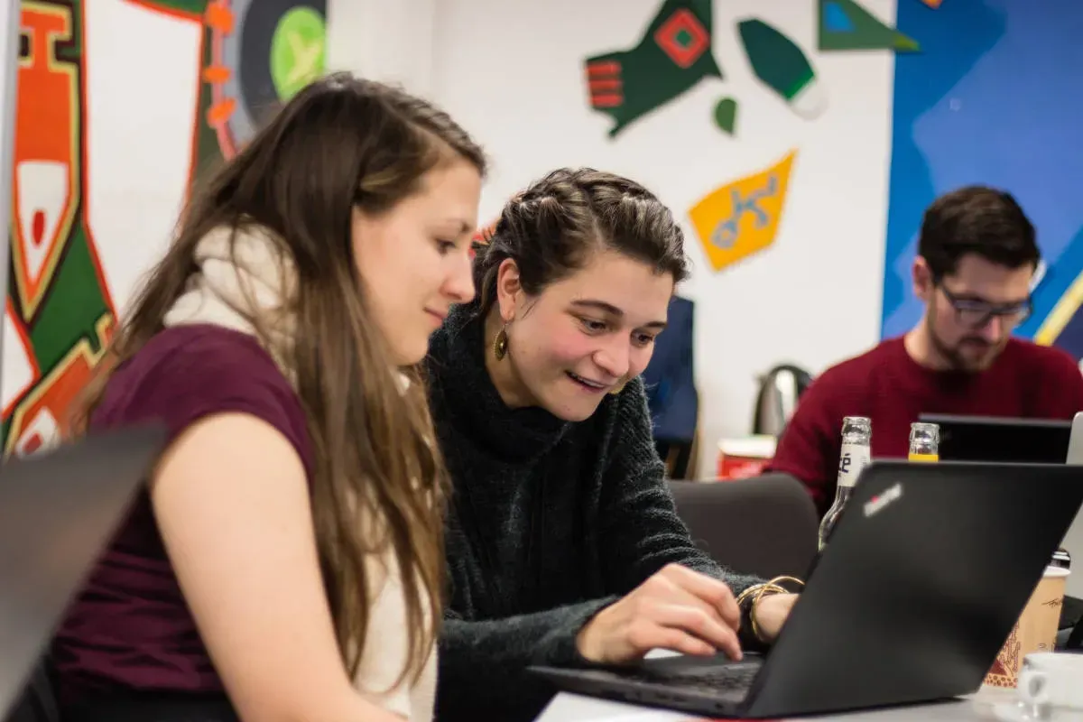 Zwei Menschen sitzen vor einem Laptop und schauen konzentriert auf etwas auf dem Bildschirm.