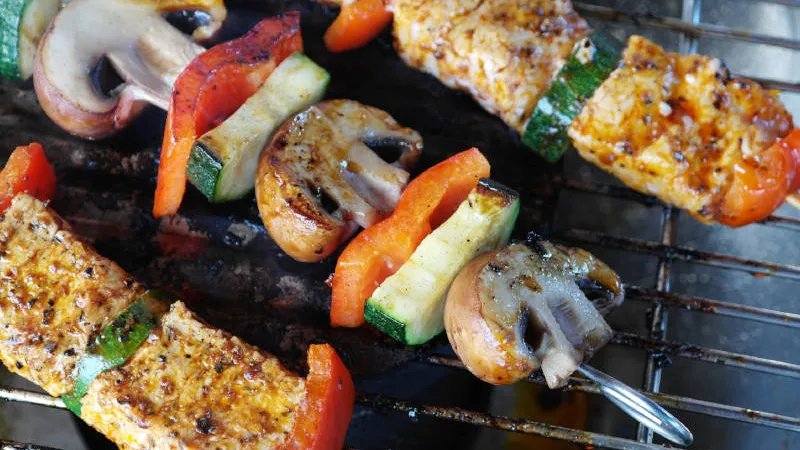 Drei Grillspieße  mit Gemüse und Tofu liegen auf einem Grill