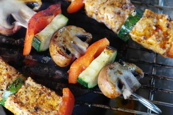 Drei Grillspieße  mit Gemüse und Tofu liegen auf einem Grill