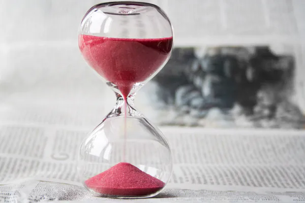 An hourglass filled with red sand, with more in the upper half than in the lower half.