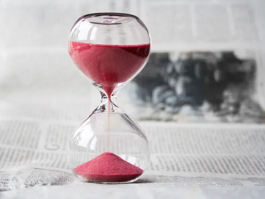An hourglass filled with red sand, with more in the upper half than in the lower half.