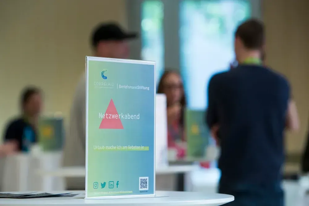 Ein DinA4 Aufsteller auf einem Stehtisch. Er ist in den CorrelAid Farben gehalten. Darauf steht 